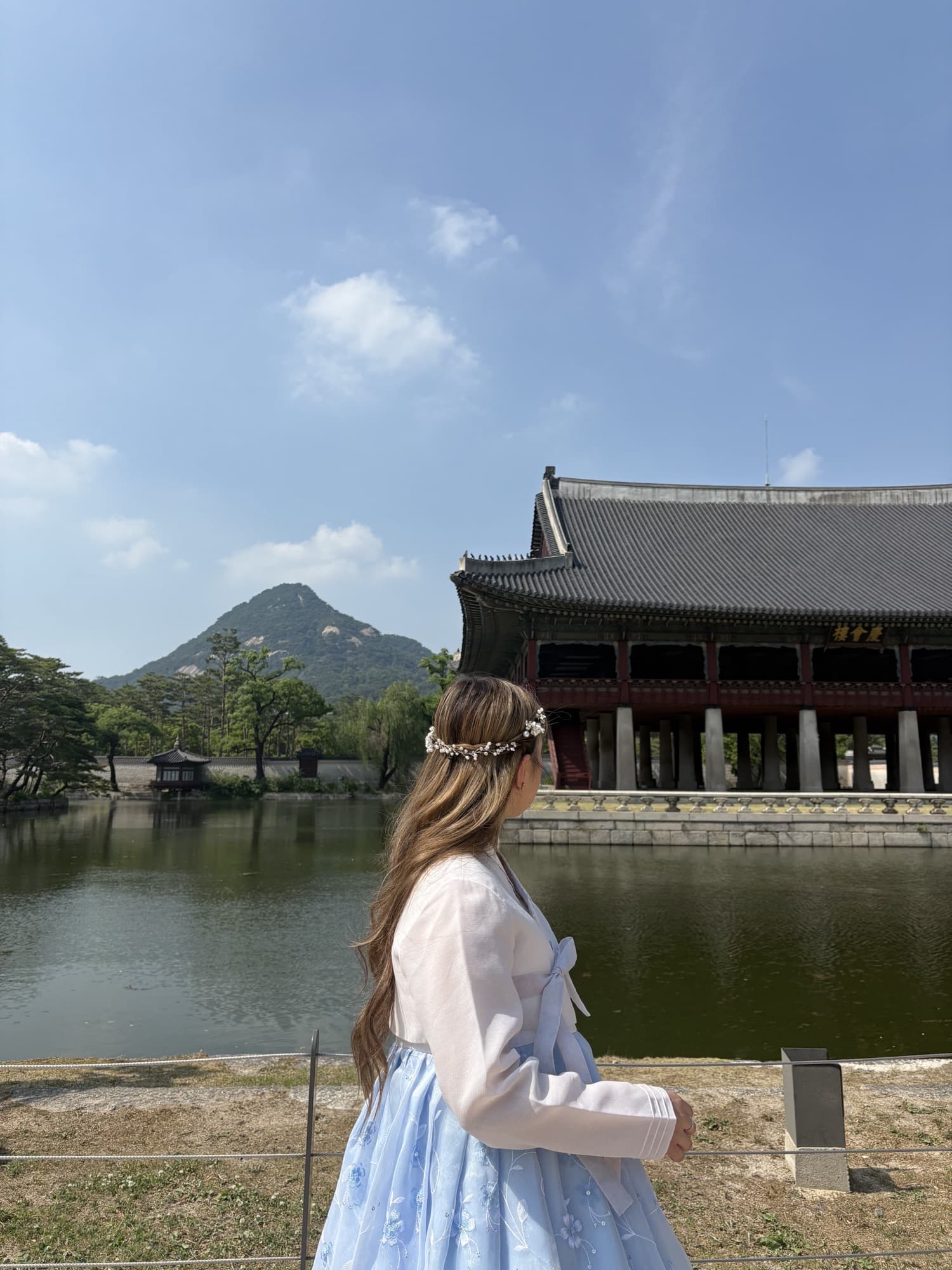 Katrina in a white dress by a pond in front of a traditional Korean palace